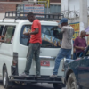 Two men riding on the back of a taxi van in Haiti