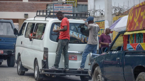 Two men riding on the back of a taxi van in Haiti