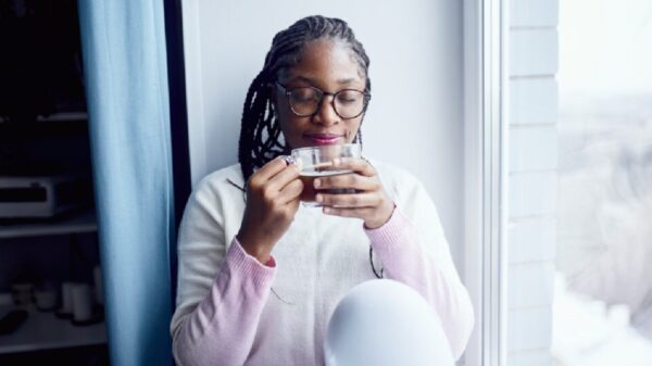 A young woman sits at the window with her eyes closed and enjoys drinking coffee