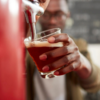 Young African bartender pouring beer in craft brewery.